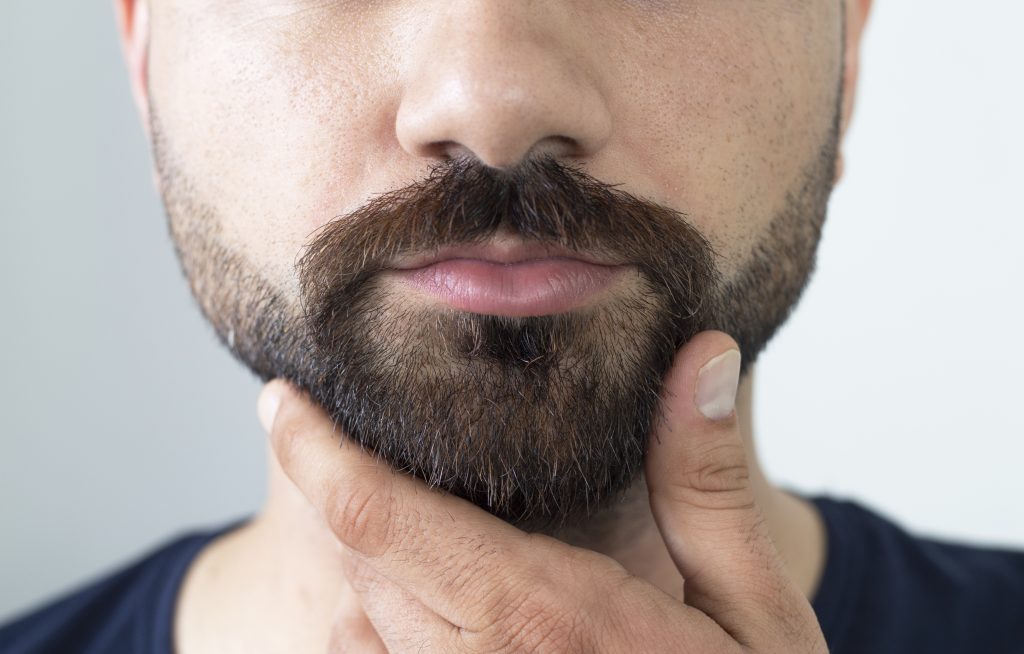 Imagen de joven barbudo tocándose la barba de pie. Clínica especializada en injerto capilar y tratamientos estéticos en Madrid