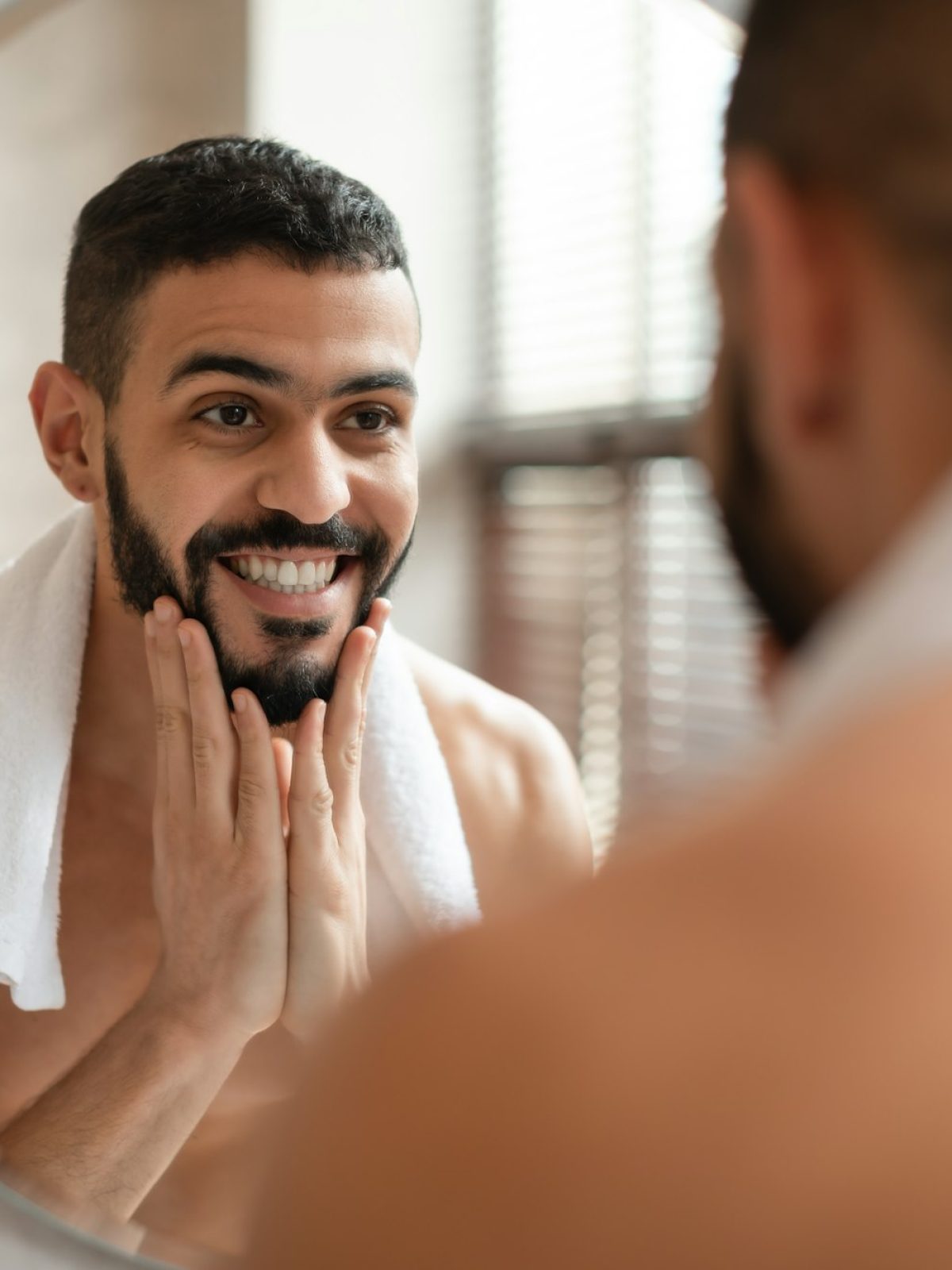 Confident young Arab guy looking in the mirror, touching beard